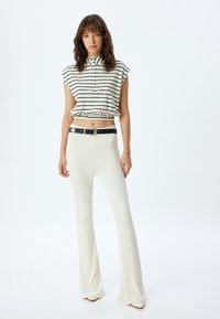 Gestreepte crop top met hoge kraag en elastische zoom, gecombineerd met ribbelige, uitlopende witte broek. Zwarte riem met zilveren gespaccenten.