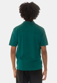 Polo shirt teal con maniche corte, colletto a coste e orlo dritto. Il materiale sembra avere una texture. Modello mostrato di spalle.