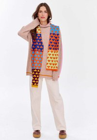 Pletený ružový sveter a farebná šatka s motívom srdiečok, kombinované s krémovými nohavicami a hnedými topánkami, so širokým strihom a pohodlnou textúrou.