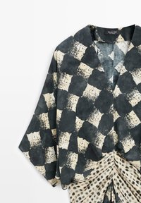 Schwarz-weiß abstrakt gemusterte Kimono-Bluse mit weiten Ärmeln und einem gerafften karierten Detail am Saum.