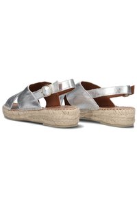 Silver metallic sandals with a woven jute sole, open design, adjustable buckle strap, and cut-out details on the sides.