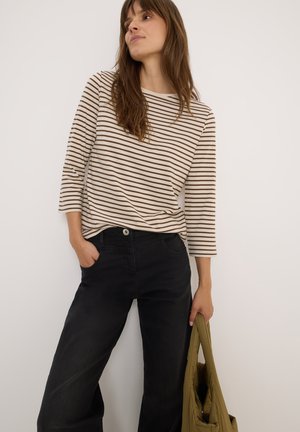 Chemise à rayures à manches longues en crème et marron, accompagnée d'un jean noir à larges jambes. Le modèle tient un sac vert olive. Design simple et décontracté.