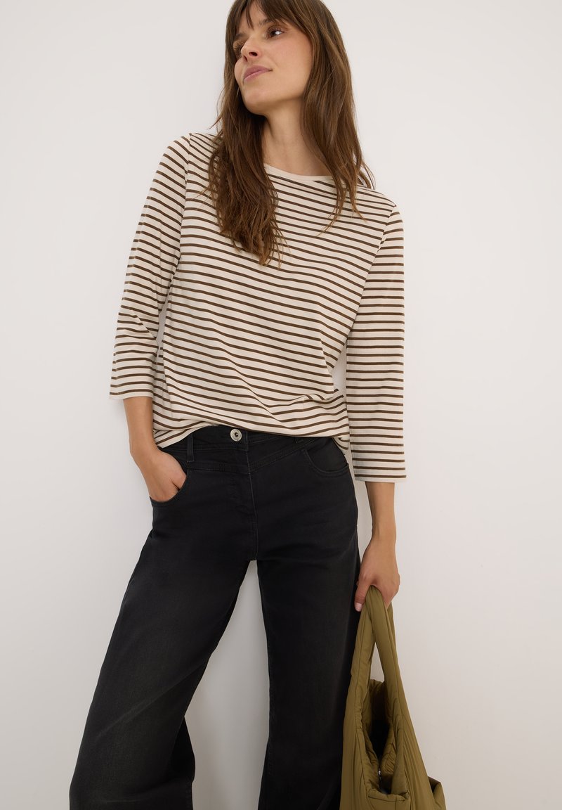 Chemise à rayures à manches longues en crème et marron, accompagnée d'un jean noir à larges jambes. Le modèle tient un sac vert olive. Design simple et décontracté.