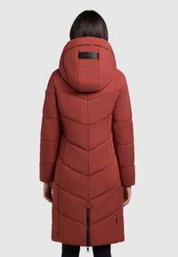 Raudona pūsta striukė su pūstais raštais ir gaubtu. Turi įstrižus siuvimo raštus ir užtrauktuką apačioje. Nugaros vaizdas.