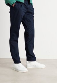Pantalons bleu marine en tissu lisse, coupe ajustée, associés à des baskets blanches au design minimaliste et à semelles textur�ées.
