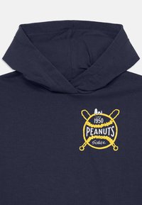 Jūras spēku kapuce ar priekšējo grafiku, kas satur dzeltenu tekstu, beisbola motīvu un Snoopy ilustrāciju. Mīksts audums ar brīvu piegriezumu.