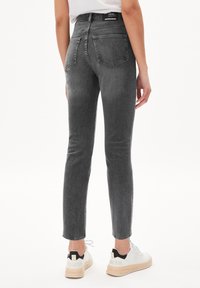 Jean gris taille haute à coupe slim, avec cinq poches et coutures visibles, associé à des baskets blanches avec des touches noires.