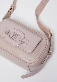 Borsa in pelle rosa chiaro con forma rettangolare, superficie texture e un particolare fermo prominente. Presenta una tracolla regolabile in tono beige.