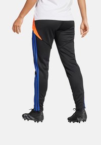 Schwarze Sporthose mit blauen Streifen an den Seiten und einem orangefarbenen Akzent an der hinteren Tasche, aus glattem, elastischem Material gefertigt.