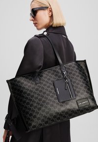 Borsa a tracolla nera con motivo a fulmine impresso, texture liscia e dettagli in pelle. Presenta una pochette con zip sospesa e un'etichetta con logo.
