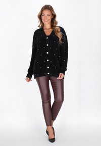 Black fuzzy cardigan with white buttons and scattered rhinestones, paired with dark burgundy fitted pants and black heels.