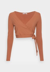 Top cropped em cor ferrugem com mangas longas, apresentando um decote em V e um detalhe de nó atado na cintura. Feito de um tecido suave e elástico.