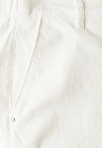 White cotton pants featuring a smooth texture, stitched seams, zipper fly, and a silver-tone button. Minimalist design, no visible patterns.