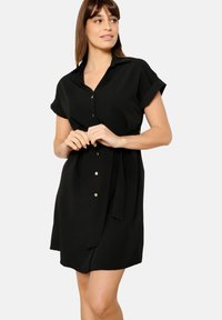 Vestito nero a camicia in tessuto leggero, con colletto, maniche corte, bottoni frontali e un accento in vita legato.