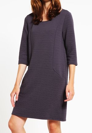 Woman wearing a knee-length, dark gray textured dress with three-quarter sleeves and a subtle side pocket detail.