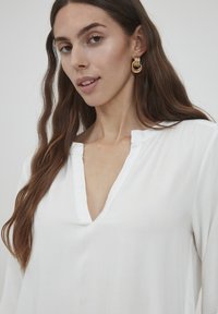 Witte, lichte blouse met een v-hals, lange mouwen en een zachte textuur. Heeft een subtiele gestikte halslijn detail.