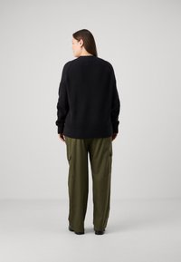 Pull noir côtelé à coupe ample, associé à un pantalon cargo olive avec poches latérales et ourlets retroussés.