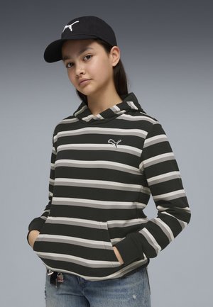 Sweat à capuche rayé noir et blanc avec une poche kangourou, doté d'une capuche et d'un petit logo sur la poitrine. Associé à un jean bleu déchiré et une casquette noire.