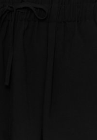 Svart, lätt tyg med en mjuk textur; har en elastisk midjeband och en dragsko för justering.