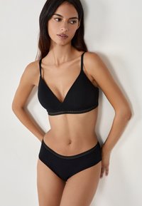 Conjunto de sujetador y braguitas a juego de color negro, hecho de tela suave. El sujetador tiene un escote en V y un delicado ribete, mientras que la braguita cuenta con una cinturilla suave.