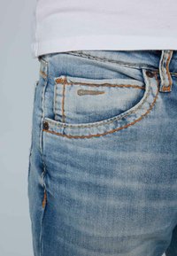 Jeans de mezclilla azul claro con costuras naranjas, un bolsillo frontal y un corte clásico con un ligero desgastado en la tela.