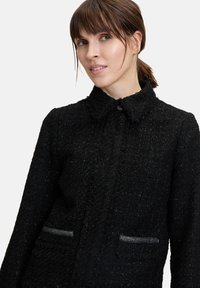 Czarna tkana kurtka o teksturowanym wykończeniu, z kołnierzykiem, zapinana na guziki z przodu oraz z kieszeniami akcentującymi delikatny połysk.