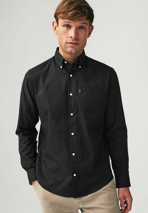 Zwarte button-up shirt met een kraag, voorzien van een borstzak en witte knopen. De stof lijkt glad met een matte afwerking.