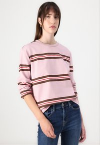 Maglietta a maniche lunghe rosa chiaro con strisce orizzontali marroni e rosse, caratterizzata da un collo rotondo e una vestibilità comoda. Abbinata a jeans blu scuro.