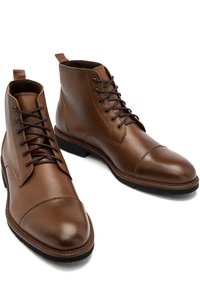 Brązowe skórzane botki za kostkę o gładkiej fakturze, okrągłym nosie i czarnych sznurówkach. Mają pętelkę z tyłu oraz teksturowaną gumową podeszwę.