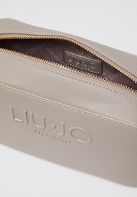 Beige synthetische pouch met een getextureerd oppervlak, voorzien van een gouden ritssluiting en geperst merklogo aan de binnenkant. Gladde binnenvoering.