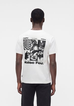 Mann trägt weißes T-Shirt mit schwarzen grafischen Panels und Text "Live Tonight... Noise Fest" auf dem Rücken, steht vor einem einfarbigen Hintergrund.