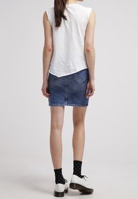 Vit ärmlös topp i kombination med en mörk denimkjol. Har en rundad nederkant, med en ficka på baksidan, och svarta strumpor med vita prickar.