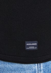 Black textured sweater with a ribbed hem and a small fabric label displaying "JACK & JONES" and "AUTHENTIC JEANSWEAR SINCE 1990."