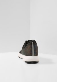 Černá sportovní obuv s texturovaným síťovaným svrškem a reflexním detailem, bílou podrážkou a hladkými konturami pro aerodynamický tvar.