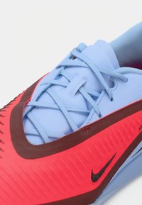 Nike athletic shoe featuring a bright red upper with textured accents, blue laces, and a striking black logo on the side.