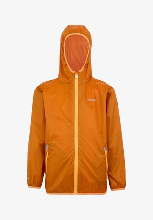 Niño sonriente con chaqueta con capucha naranja, camiseta gris con cremallera, pantalones cortos cargo oliva, calcetines amarillos y zapatillas negras sobre un fondo liso.
