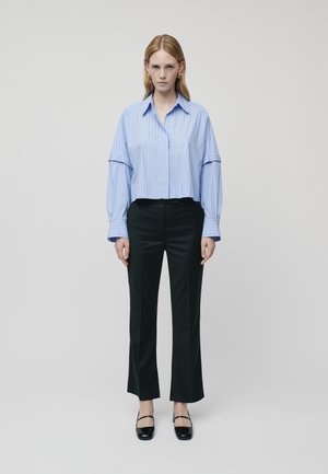 Blaue gestreifte, langärmlige Bluse, kombiniert mit schwarzen, weit geschnittenen Hosen und schwarzen flachen Schuhen. Einfaches Design und klare Linien.