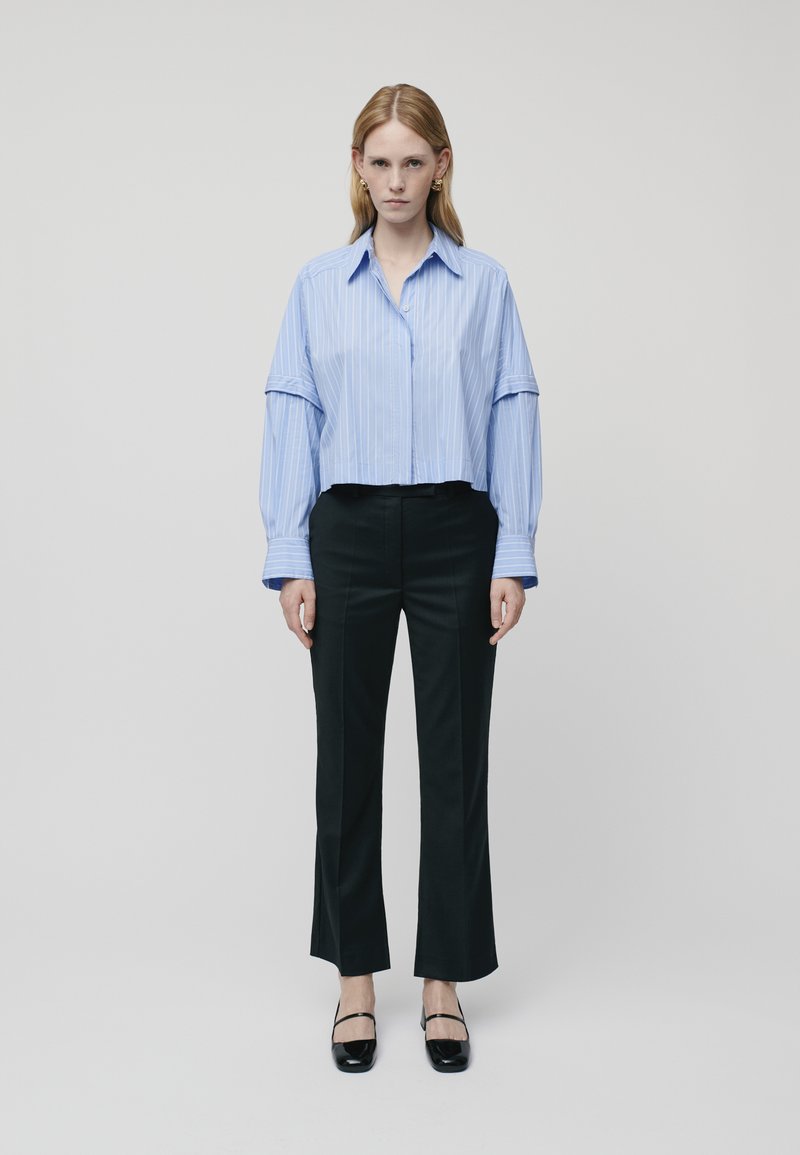 Camicia blu a righe, taglio corto e maniche lunghe, abbinata a pantaloni neri a zampa d'elefante e scarpe nere flat. Design semplice e linee pulite in tutto.