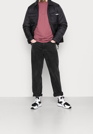 Chaqueta negra de plumas, camiseta rosa y vaqueros negros. Zapatillas en blanco y negro con un acabado texturizado. Corte relajado, con los puños de los pantalones remangados.