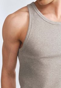 Szary, żebrowany top na ramiączkach z szerokimi ramiączkami, o dopasowanym kroju i miękkiej fakturze, częściowo pokazany na górnej części ciała modelki.