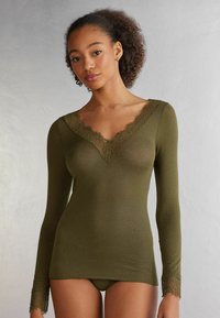 Olive green long-sleeve top with a v-neck and lace trim along the neckline and cuffs, made from a soft, sheer fabric.
