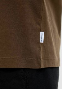 Bruine katoenen t-shirt met een lichte ribbelstructuur, voorzien van een klein wit label met de tekst "JACK & JONES" op de zijnaad.