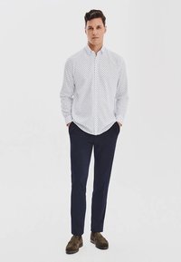 Biała koszula z guzikiem, w mały niebieski wzór kropek, granatowe spodnie i brązowe buty. Slim fit z kołnierzykiem i długimi rękawami.