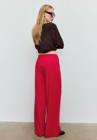 Pantaloni rosa a gamba larga con vita alta, abbinati a un top corto marrone scuro. Tessuto liscio con vestibilità rilassata, dettagli minimi e senza motivi visibili.