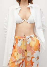 Chemise blanche boutonnée, soutien-gorge blanc, et pantalon à motifs floraux aux teintes orange et rose, avec une ceinture élastique et un cordon de serrage.