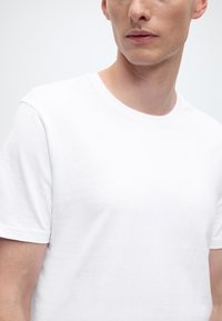 Maglietta bianca in cotone con scollo rotondo e maniche corte, caratterizzata da un design semplice e una texture liscia. Vista ravvicinata del tessuto.