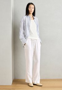 Pantalons en lin blancs avec cordon de serrage, associés à un débardeur crème clair et à une chemise à boutons bleu et blanc à rayures, ample.