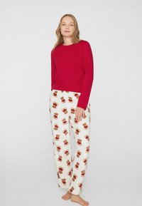 Červený top s dlouhým rukávem a kulatým výstřihem, kombinovaný s bílými kalhotami s potiskem medvídka v hnědé a červené barvě. Měkká látka, volný střih.