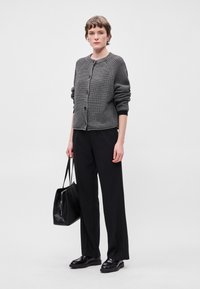 Γκρίζα πλεκτή ζακέτα με υφή, στρογγυλή λαιμόκοψη και κουμπιά μπροστά, συνδυασμένη με μαύρες ψηλές παντελόνες και μαύρη τσάντα ώμου.