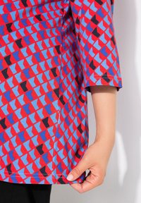 Camicia a maniche corte con motivo geometrico nei colori rosso, blu e nero; realizzata in cotone; vestibilità casual; dettagli dell'orlo visibili.